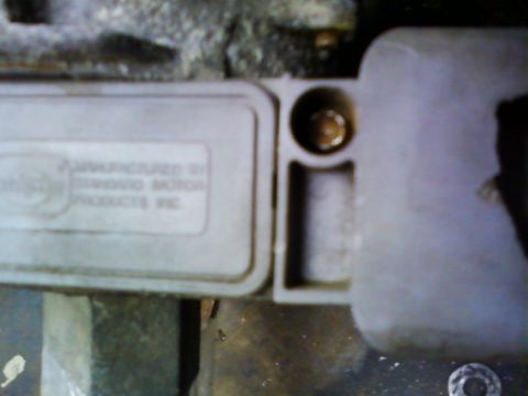 1990 Ford Bronco - Close-up of a gray plastic ignition module molded with 'Manufactured by Standard Motor Products Inc.', its mounting flange and slotted scre…