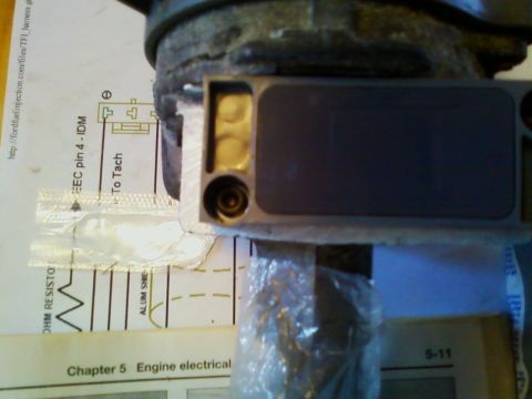 1990 Ford Bronco - A gray TFI ignition control module with gold spade terminals and a round connector, resting on a printed Ford fuel-injection wiring diagram…