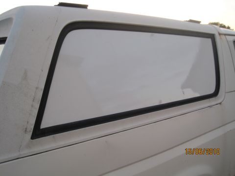 1989 Ford Bronco - A close-up view of the rear side of a white SUV, focusing on the window and body panel. The image includes a date stamp.