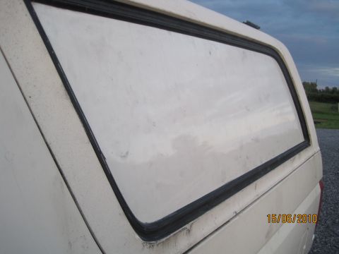 1989 Ford Bronco - Rear window of a white truck cap, showing the trim and cloudy sky.