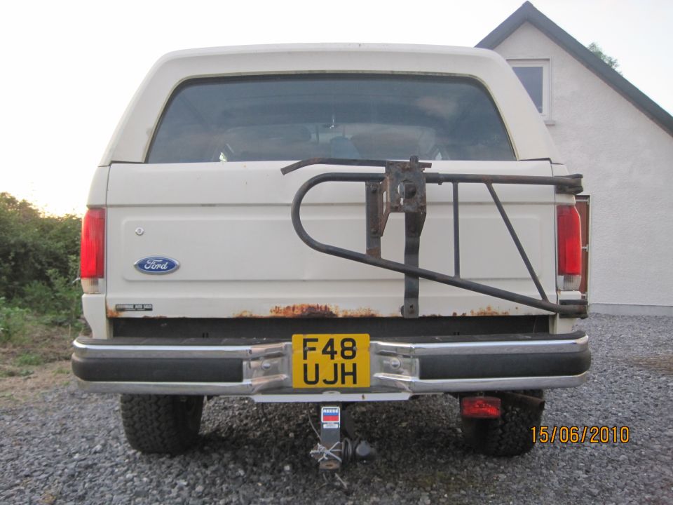 White Ford Bronco rear view, showing a spare tire carrier, yellow license plate F48 UJH, and rust on the tailgate