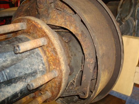 1995 Ford Bronco - Close-up view of a rusty rear axle drum brake assembly, showing wear and corrosion on the brake shoes and drum.