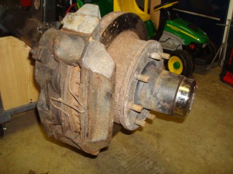 1995 Ford Bronco - This photo shows a vehicle's rear axle assembly, including the brake caliper and rotor, with a riding mower in the background.
