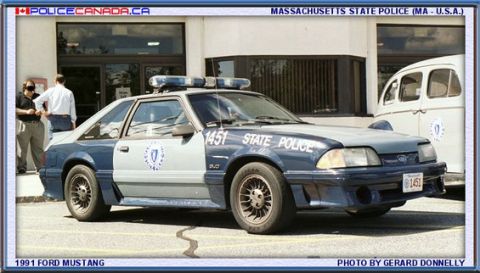 1998 Ford Crown Victoria - Massachusetts State Police car, a 1991 Ford Mustang, parked in front of a building.