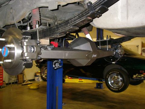 1990 Ford Bronco - The rear axle and suspension of a vehicle are shown, with another car in the background.