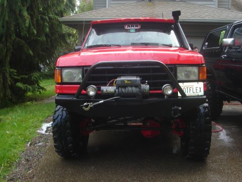 1989 Ford Bronco - Front view of a red 1989 Ford Bronco modified for off-roading, parked next to another vehicle.