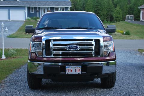 1984 Ford Bronco - Front view of a red Ford F-150 pickup truck, a chrome grille and license plate COW 106.