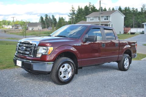1984 Ford Bronco - Maroon Ford F-150 pickup truck parked outside a residential house.