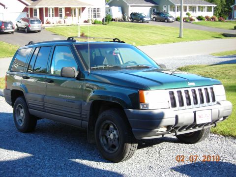1984 Ford Bronco - A green Jeep Grand Cherokee is parked in front of a suburban house on a sunny day.