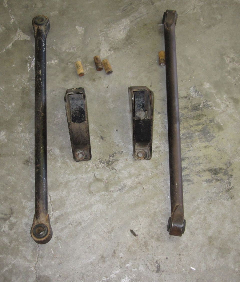 Two control arms, two mounting brackets, and four bushings on a concrete floor