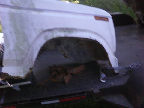 1989 Ford Bronco - The front fender and wheel well of a white pickup truck are visible, mounted on a trailer.