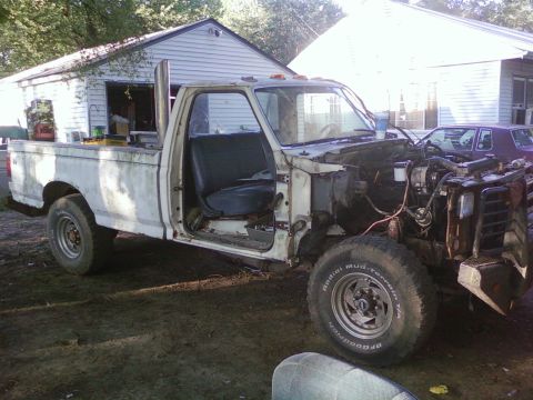 1989 Ford Bronco - This white pickup truck is missing its front end, revealing the engine compartment and various hoses.