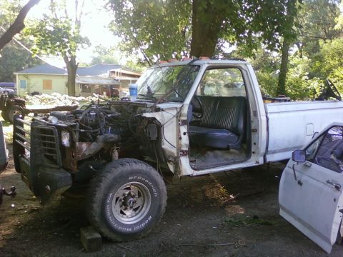 1989 Ford Bronco - White pickup truck in a yard, appearing to be undergoing repairs or disassembly.