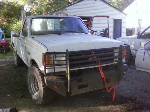 1989 Ford Bronco - This white Ford F-250 truck is equipped with a brush guard and snorkel exhaust, parked in a yard with other vehicles.