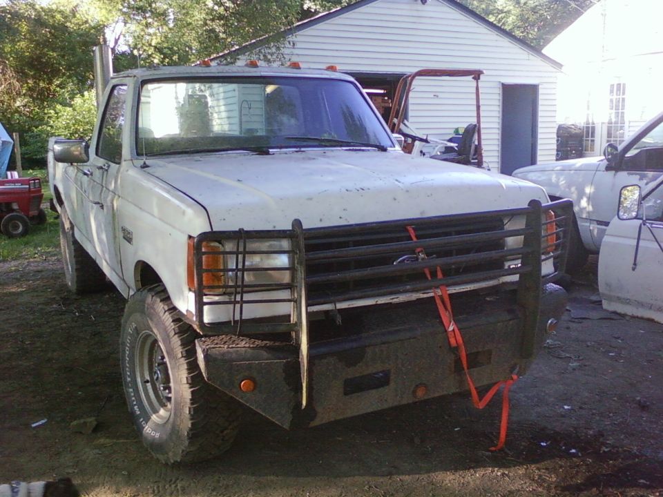 White Ford F-250 truck with a large brush guard and snorkel exhaust, parked in a yard