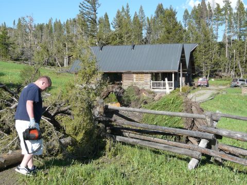 2006 Ford E350 - A man stands near a damaged fence and fallen trees, with a log cabin and two vehicles visible in the background.