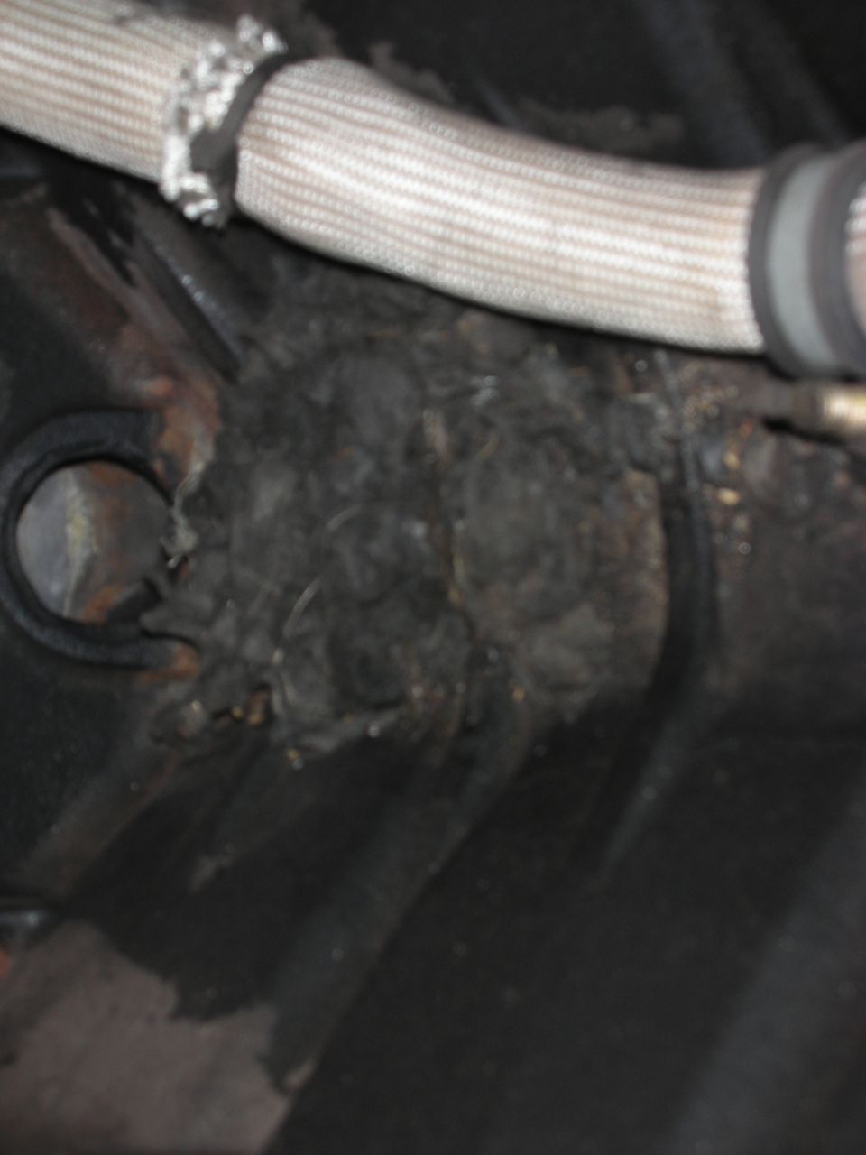 Close-up of a hose with frayed insulation and a buildup of dark, matted debris in an engine bay