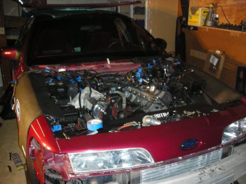 1992 Ford Crown Victoria - The engine bay of a car is shown with the hood removed, revealing complex wiring and engine components during a rebuild.