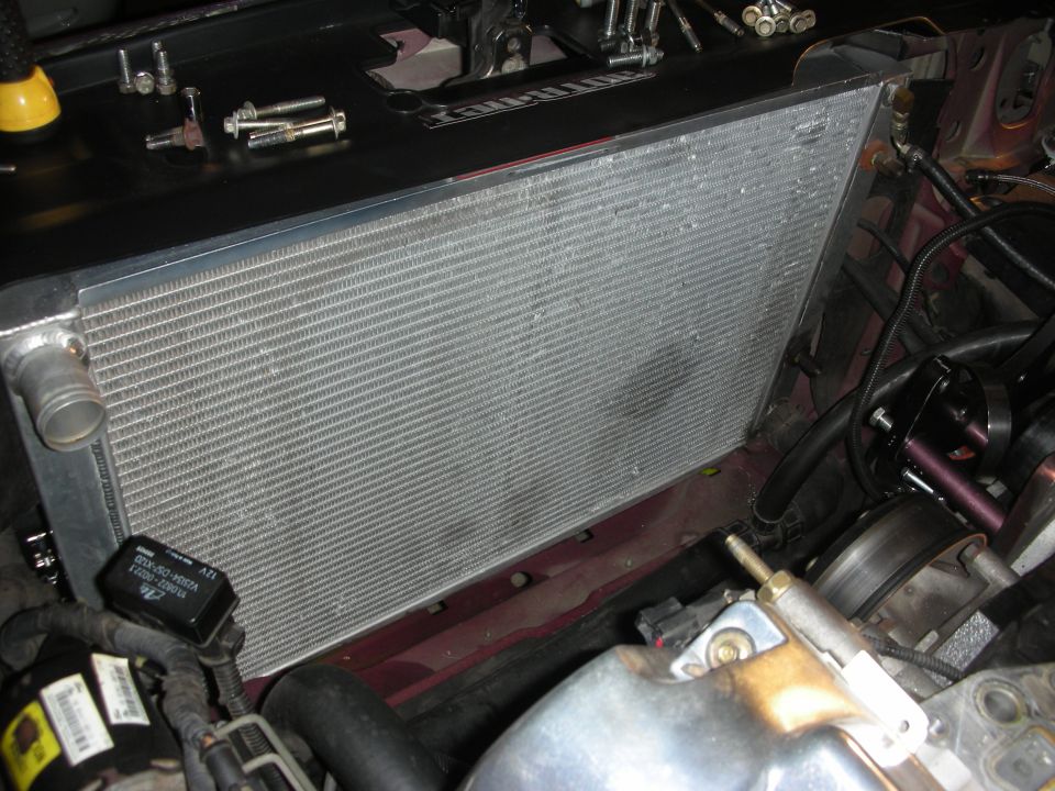 Radiator and engine parts in a vehicle engine bay, with tools on top