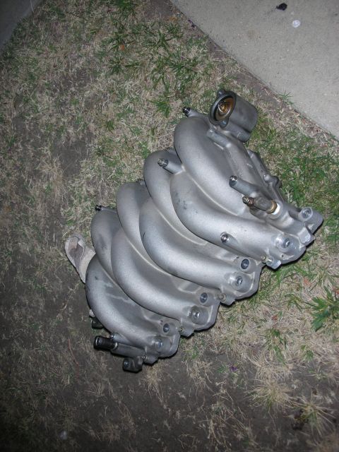 1992 Ford Crown Victoria - Aluminum intake manifold with multiple runners, resting on grass and concrete.