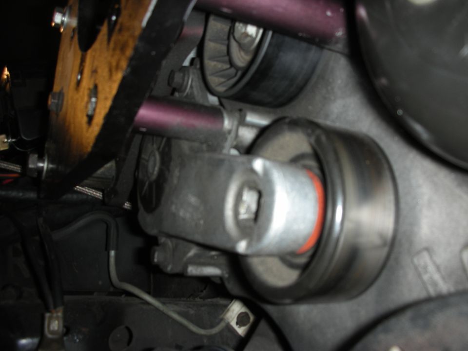Close-up of an engine belt tensioner assembly with a red seal