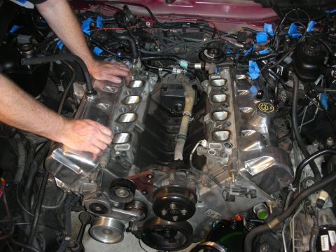 1992 Ford Crown Victoria - Mechanic's hands are shown working on a V8 engine during a rebuild, with intake manifolds removed and wiring exposed.