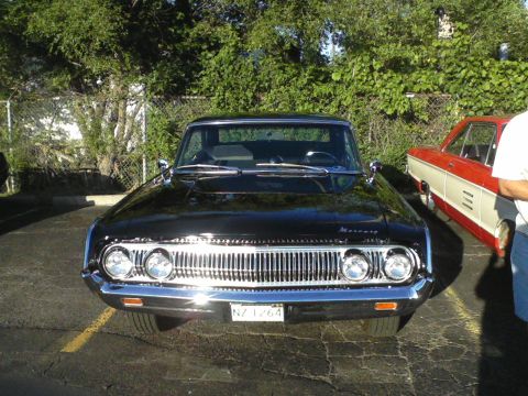 1960 Ford Falcon - This black Mercury sedan features a distinctive chrome grille and dual headlights, with another car visible to its side.