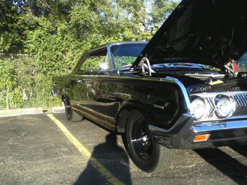 1960 Ford Falcon - A black 1965 Mercury Comet is parked outside with its hood raised, revealing the engine bay.