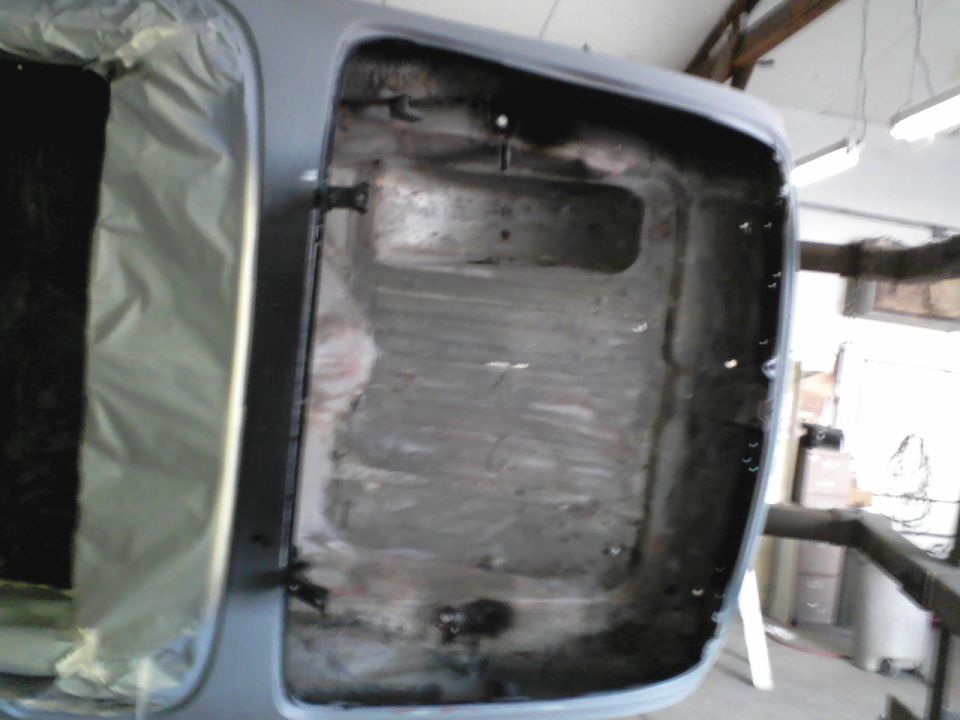 Open trunk of a gray-primered car showing bare ground-down trunk floor in a shop