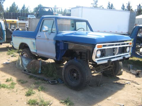 1978 Ford Bronco - This blue and white pickup truck, likely a 1975 model, is missing its front end and appears to be in a junkyard.