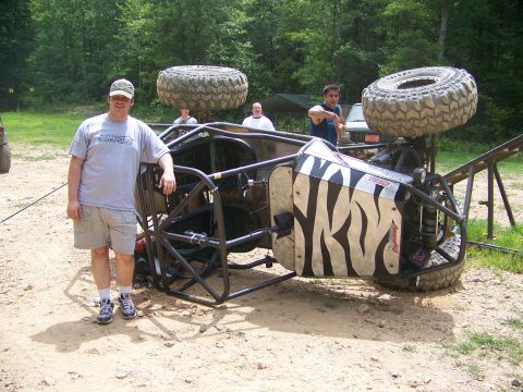 1992 Jeep YJ - A man stands next to an overturned off-road buggy with a distinctive tiger stripe paint job.