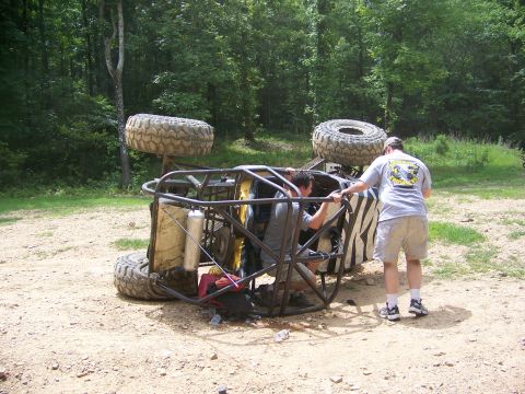 1992 Jeep YJ - Two people attempt to right an overturned off-road buggy in a wooded area.