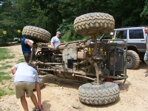 1992 Jeep YJ - An off-road buggy lies overturned on its side with several people attending to it, while a Jeep Cherokee is parked nearby.