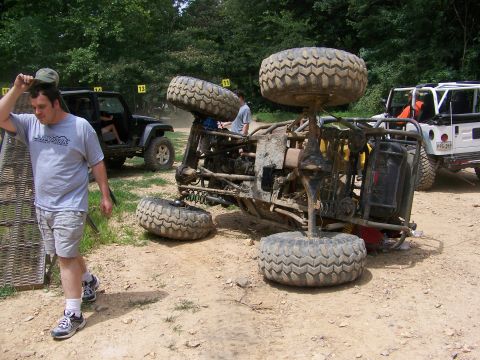 1992 Jeep YJ - An off-road vehicle has overturned on a dirt track, with other vehicles and onlookers present.