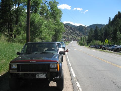 1978 Ford F-150 - A Jeep Cherokee XJ is parked on the side of a road in a mountainous area, with other vehicles visible in the distance.