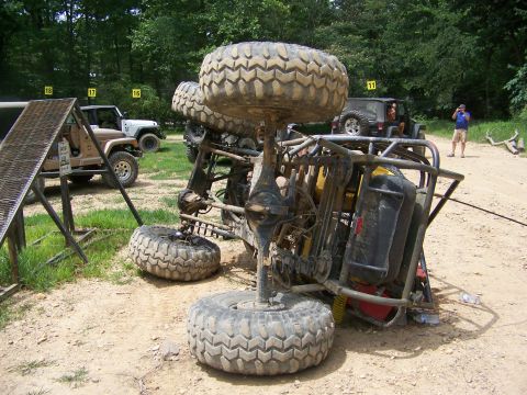 1992 Jeep YJ - An off-road buggy has flipped onto its side on a dirt path, with other vehicles and spectators in the background.