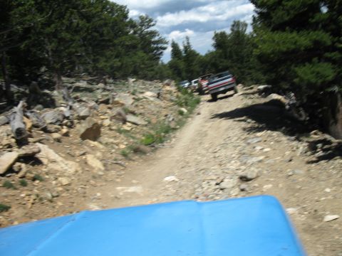 1978 Ford F-150 - Multiple trucks navigate a challenging dirt road through a rocky, wooded mountain landscape.