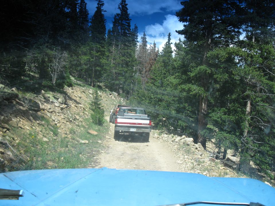 1978 Ford F-150 and another pickup truck driving on a dirt road in a forest