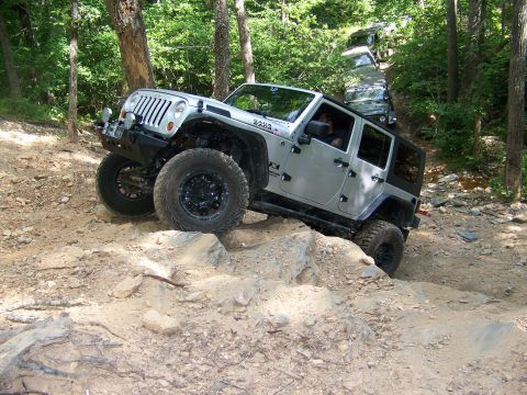 1992 Jeep YJ - Multiple Jeeps drive off-road on a wooded trail, with one vehicle climbing over large rocks.