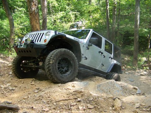 1992 Jeep YJ - Silver Jeep Wrangler tackling an off-road trail, with a second vehicle partially visible amongst the trees.