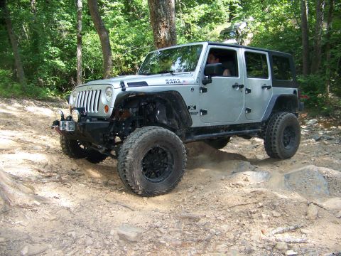 1992 Jeep YJ - A silver Jeep Wrangler JK navigates a rocky off-road trail surrounded by trees.