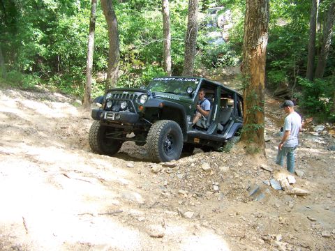1992 Jeep YJ - A green Jeep Wrangler JK navigates a challenging off-road trail with two individuals present.