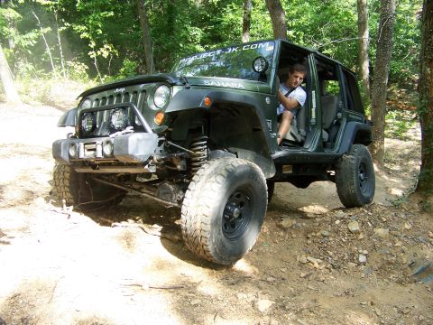 1992 Jeep YJ - Off-road Jeep Wrangler navigating a wooded trail with a driver at the wheel.