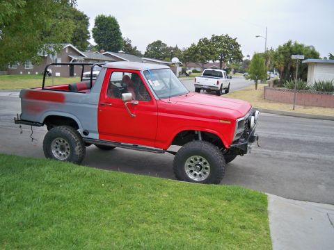 1985 Ford Bronco - This lifted SUV, possibly a Ford Bronco, is in a state of repair with one side painted red and the other grey.