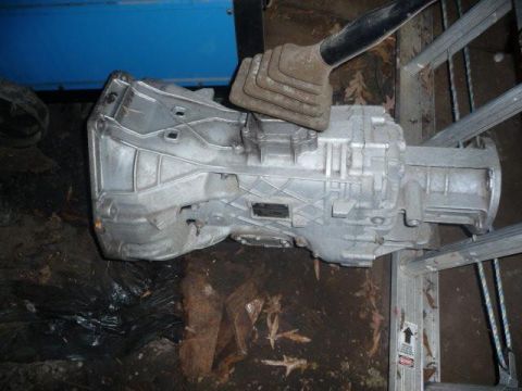 1990 Ford Bronco - A silver transmission assembly with a black shifter boot is shown, resting on metal supports.