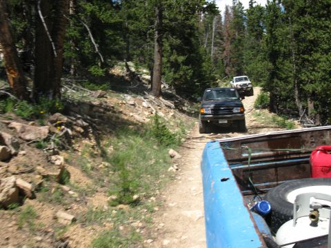1978 Ford F-150 - Several SUVs navigate a winding dirt path through a dense forest, with the camera perspective from the bed of a pickup truck.