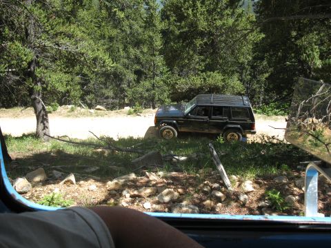 1978 Ford F-150 - Black Jeep Cherokee XJ parked on a dirt road in a wooded area.