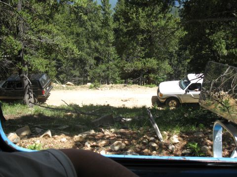 1978 Ford F-150 - Two trucks are parked on a dirt road surrounded by trees and rocky terrain.
