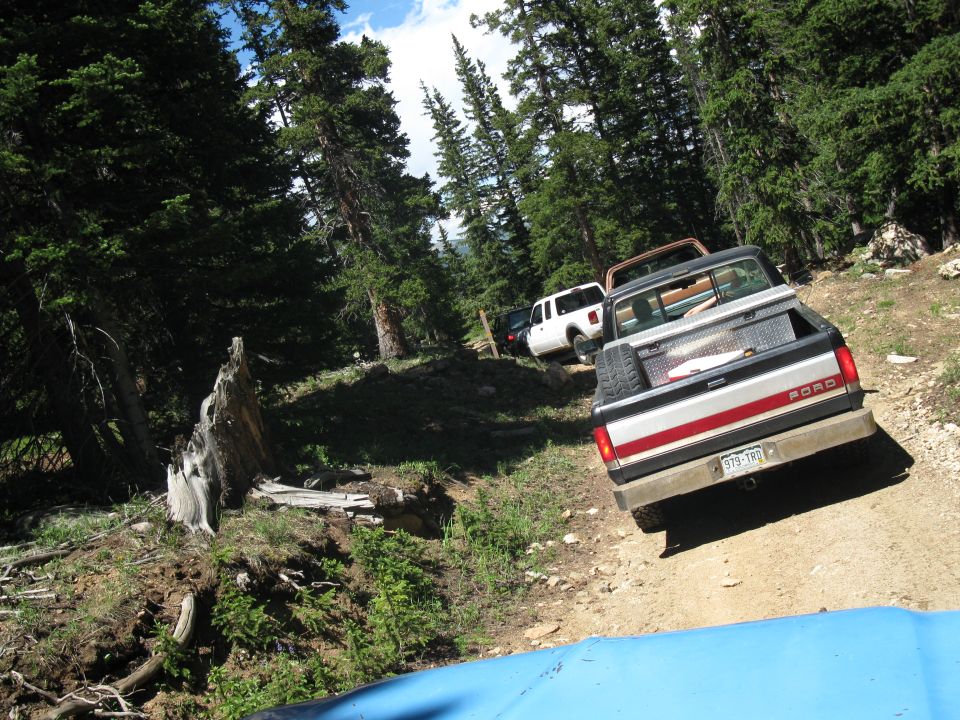 Silver and red Ford pickup truck with a toolbox in the bed, driving on a dirt road