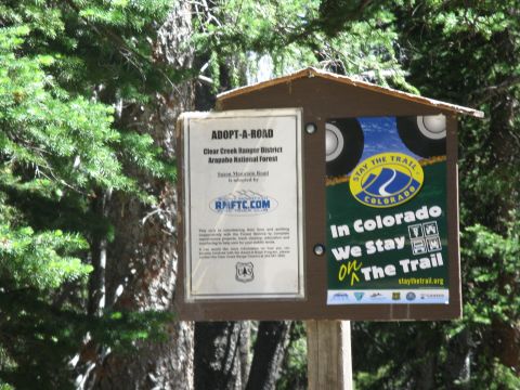 1978 Ford F-150 - A sign in a wooded area provides information about road adoption and trail etiquette in Colorado.
